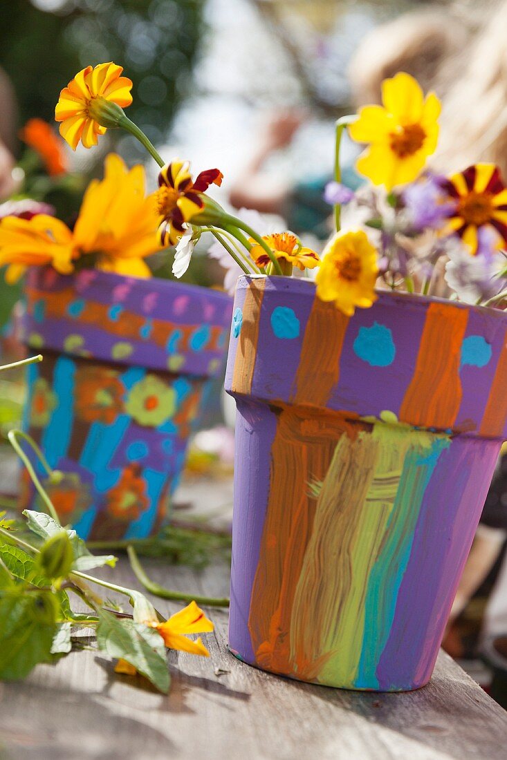 Kindlich bunt bemalte Tontöpfe mit blühenden gelben Blumen geschmückt