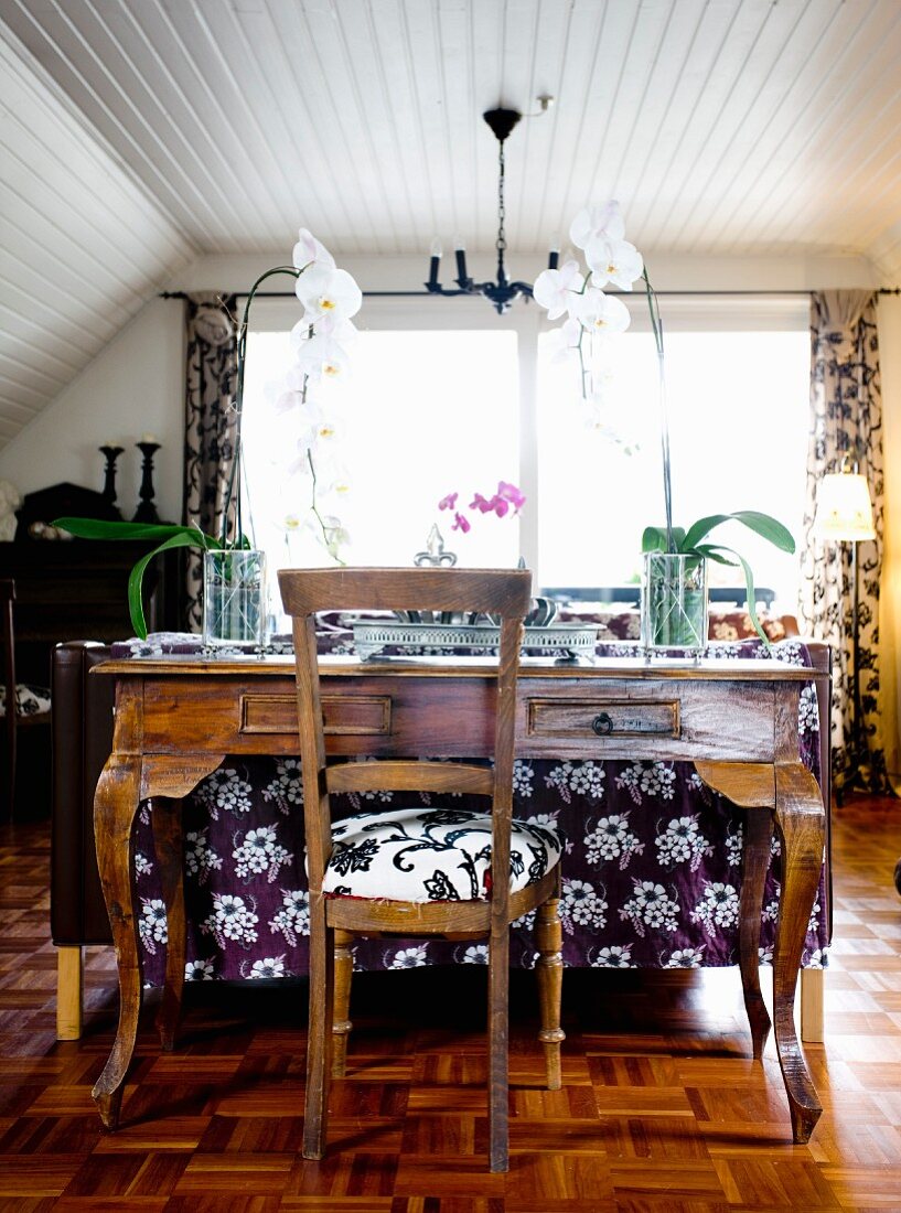 Antiker Mahagoni Schreibtisch mit Orchideen und Stuhl in ländlichem Wohnzimmer, mit weisser Holzverkleidung teilweise an Wand und Decke