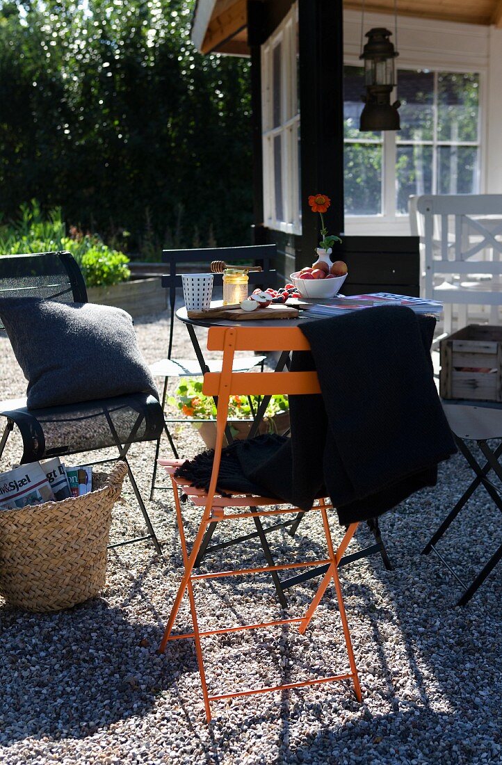 Plaid und Kissen auf farbigen Klappstühlen auf gekiestem Boden im Garten