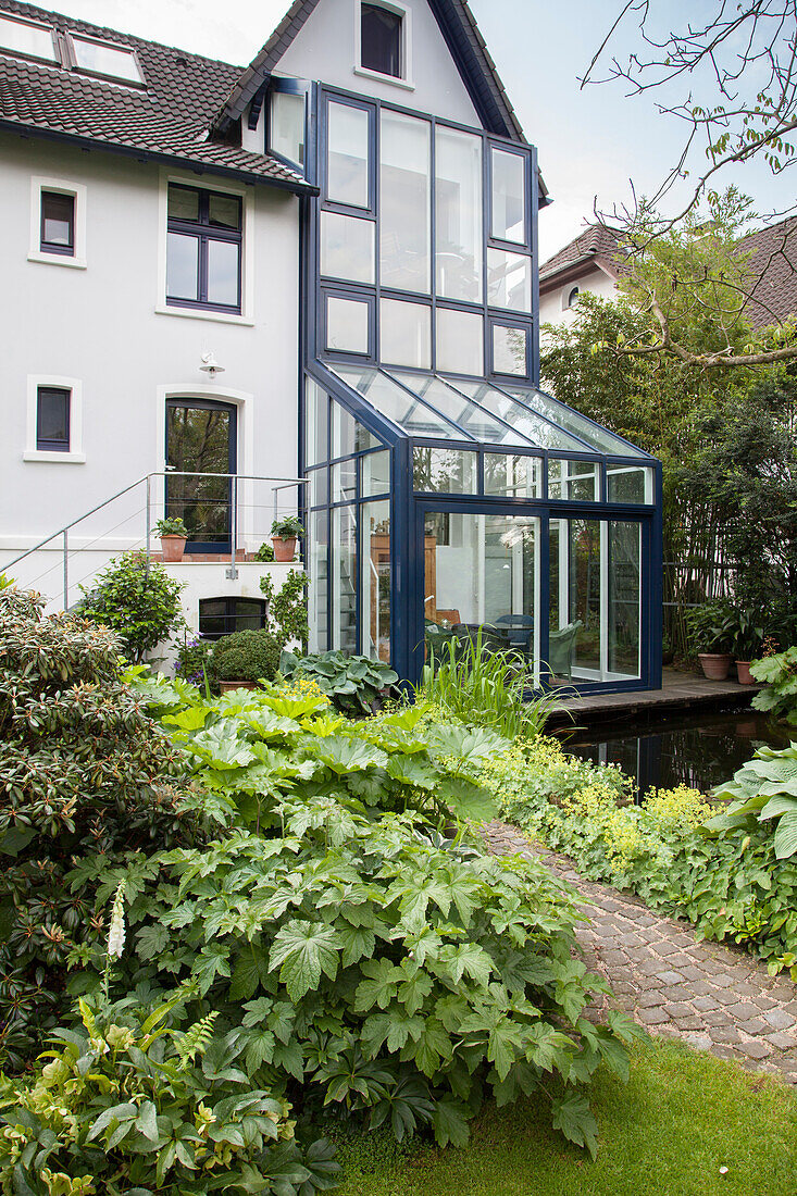 Bushes in various shades of green in front of house with blue steel and glass conservatory structure