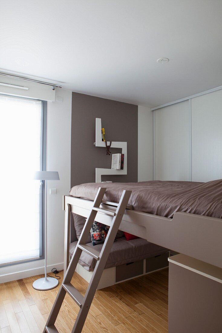 Ladder leading to loft bed lowered over sofa with drawers