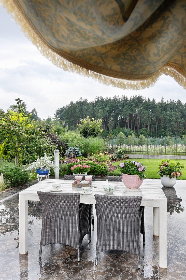 Esstisch und graue Rattanstühle auf Terrasse mit poliertem Marmorbelag