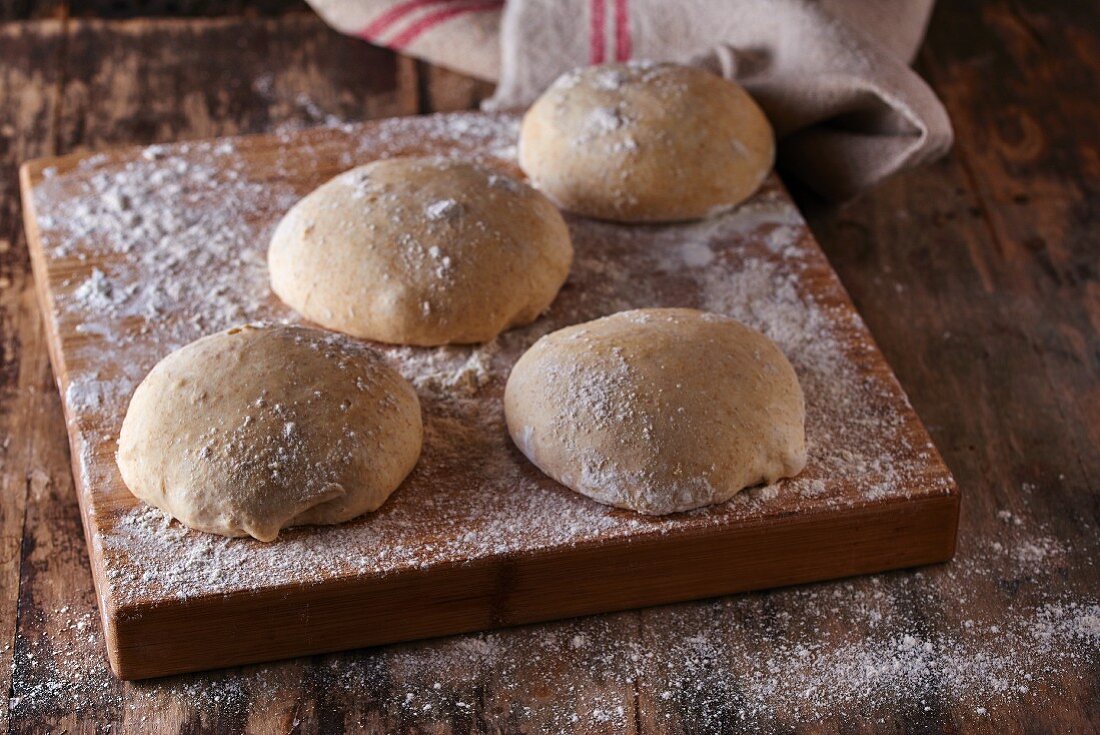 Portions of unbaked bread dough on a floured wooden platter