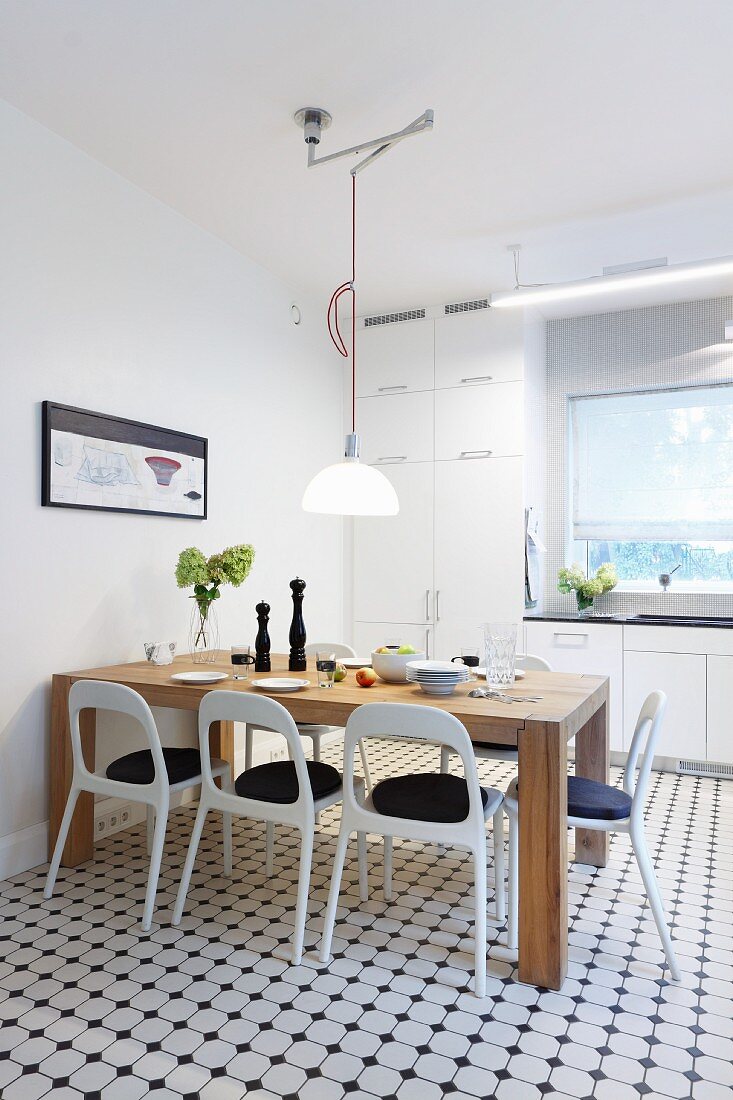 Solid wooden table and white retro chairs in modern kitchen with white and grey mosaic floor tiles