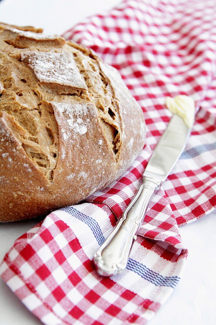 Crusty bread and a knife with butter on a checked cloth