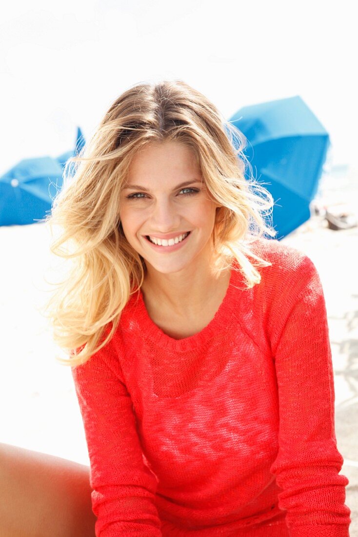 A young blonde woman on a beach wearing a transparent red knitted jumper