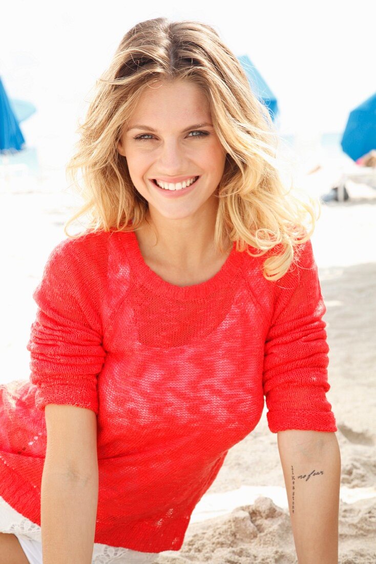 Junge blonde Frau in transparentem roten Strickpulli am Strand