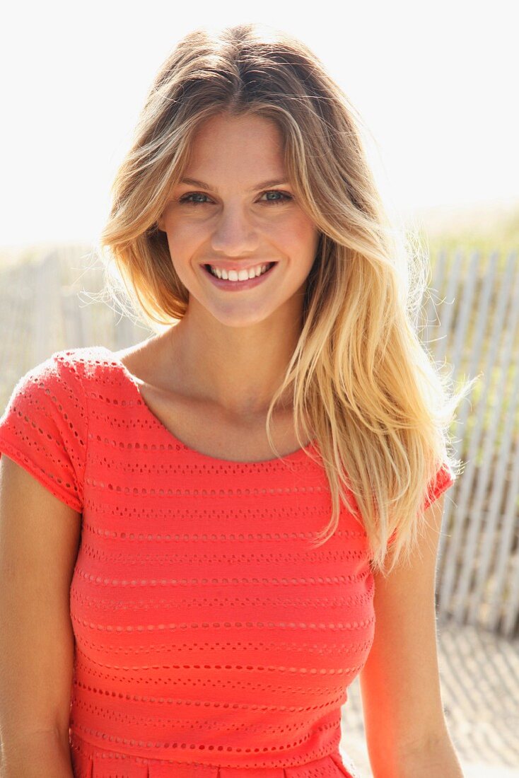 A young blonde woman on a beach wearing a salmon-coloured top