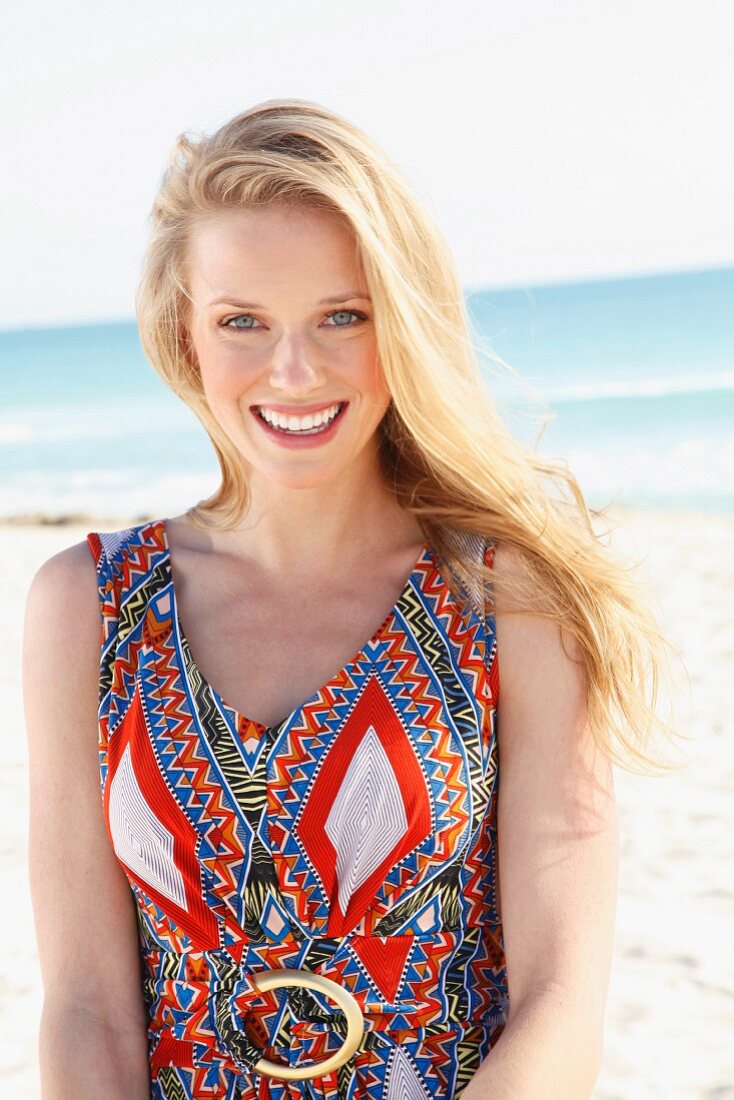 A young blonde woman on a beach wearing an ethnic patterned summer dress