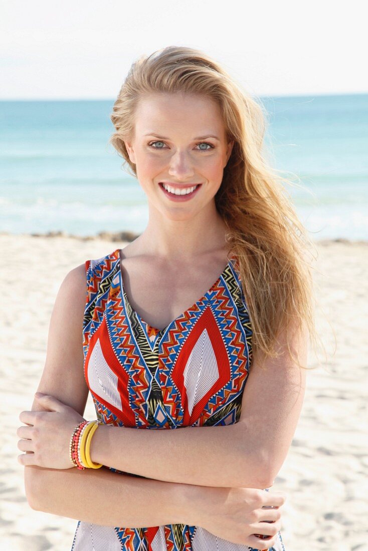 A young blonde woman on a beach wearing an ethnic patterned summer dress