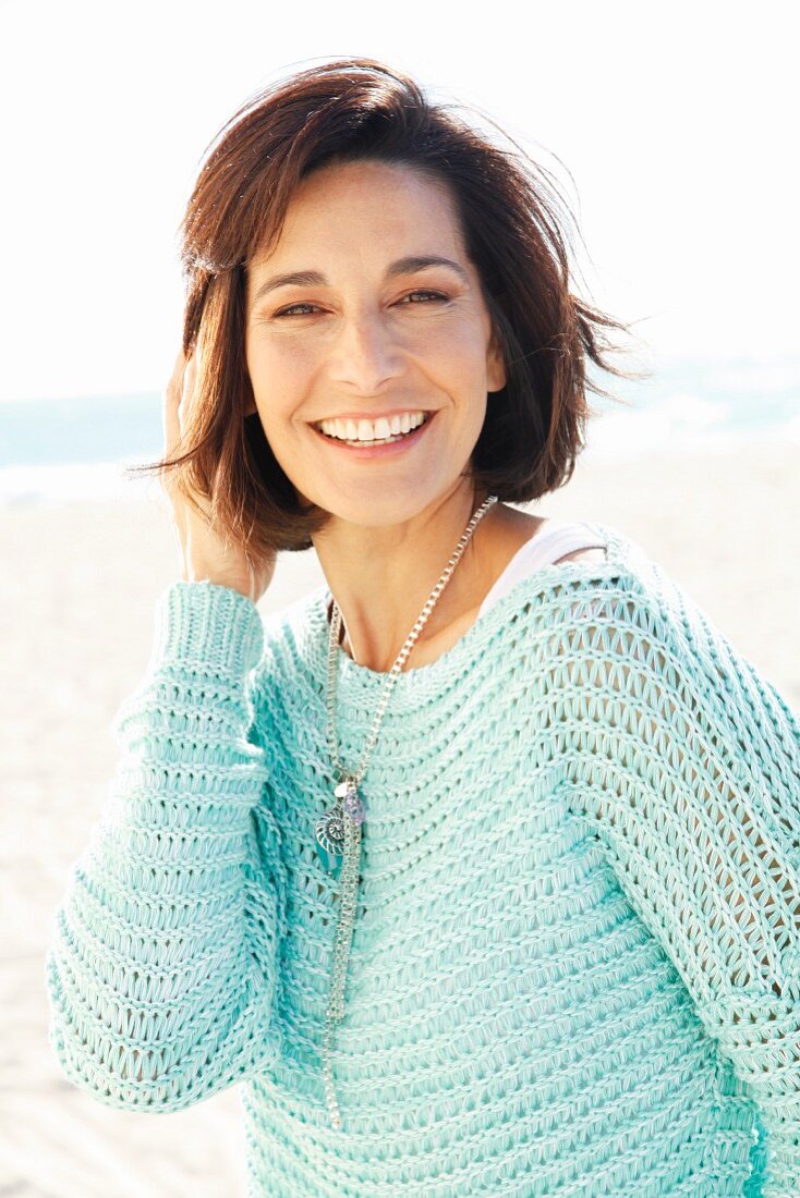 Brunette woman wearing white top and loosely knitted mint sweater on beach