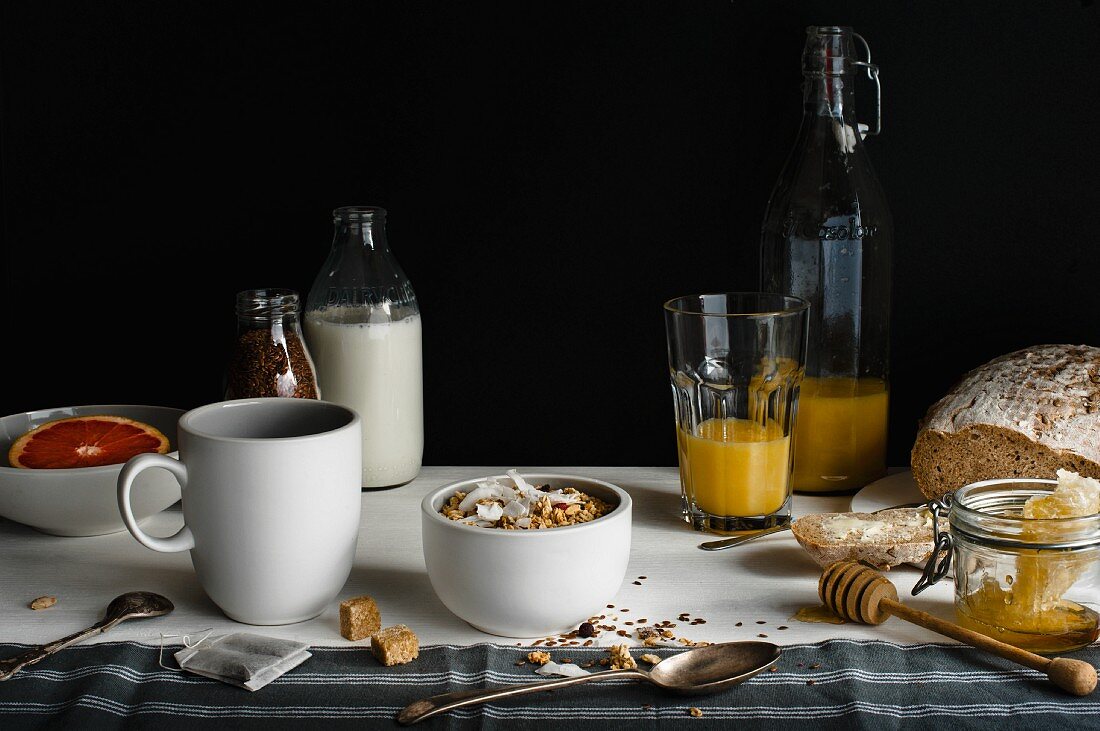 Frühstückstisch mit Milch, Cerealien, Orangensaft, Brot, Honig und Grapefruit