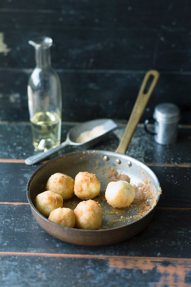 Mini potato dumplings being rolled in breadcrumbs