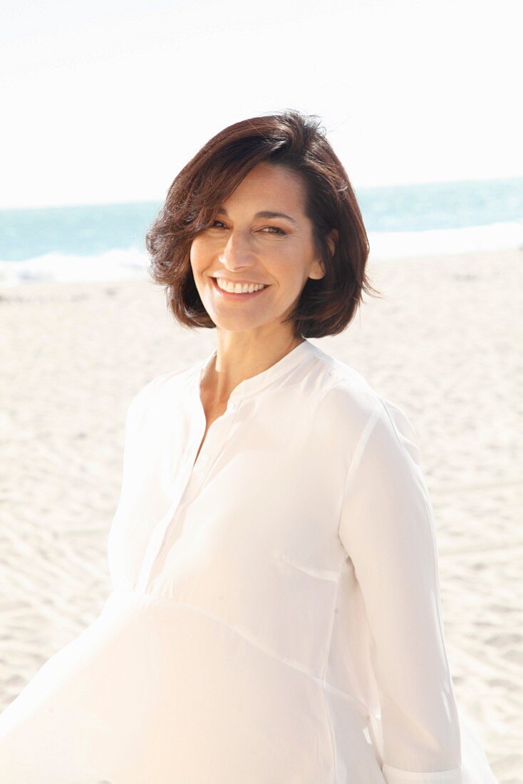 A brunette woman on a beach wearing a thin white blouse