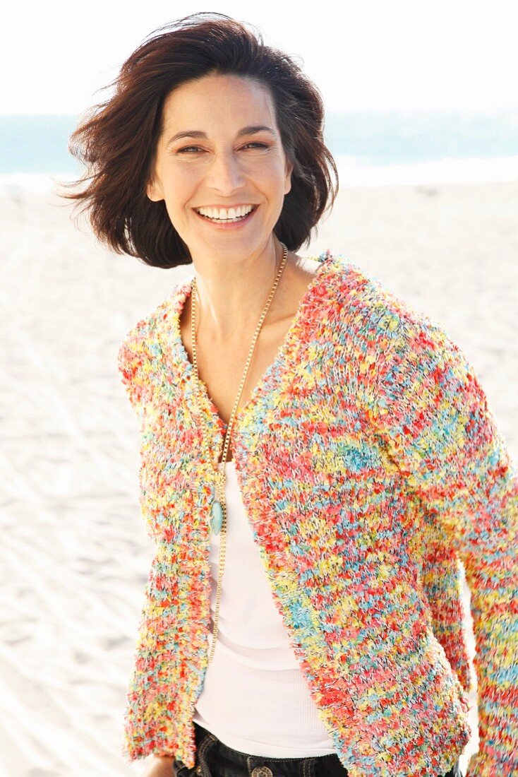 Brünette Frau in weißem Shirt und bunter Strickjacke am Strand