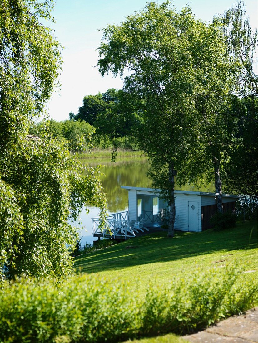 Modernes weißes Seehäuschen mit Holzterrasse an malerischem See im Sommer