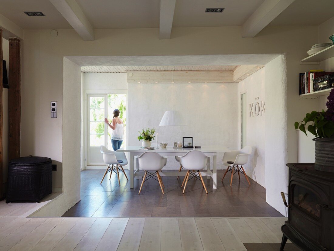 Sunken dining area with tiled floor, designer chairs and woman standing in open terrace doors in renovated country house