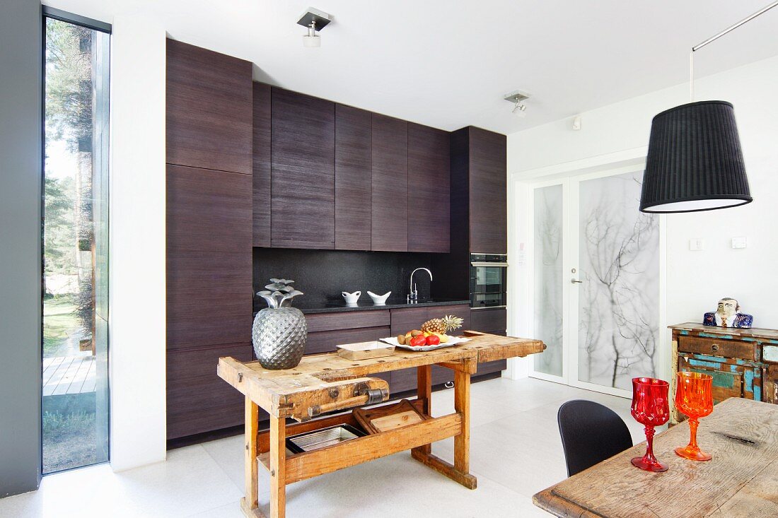 Old workbench used as rustic island counter in front of modern, charcoal grey kitchen in open-plan interior