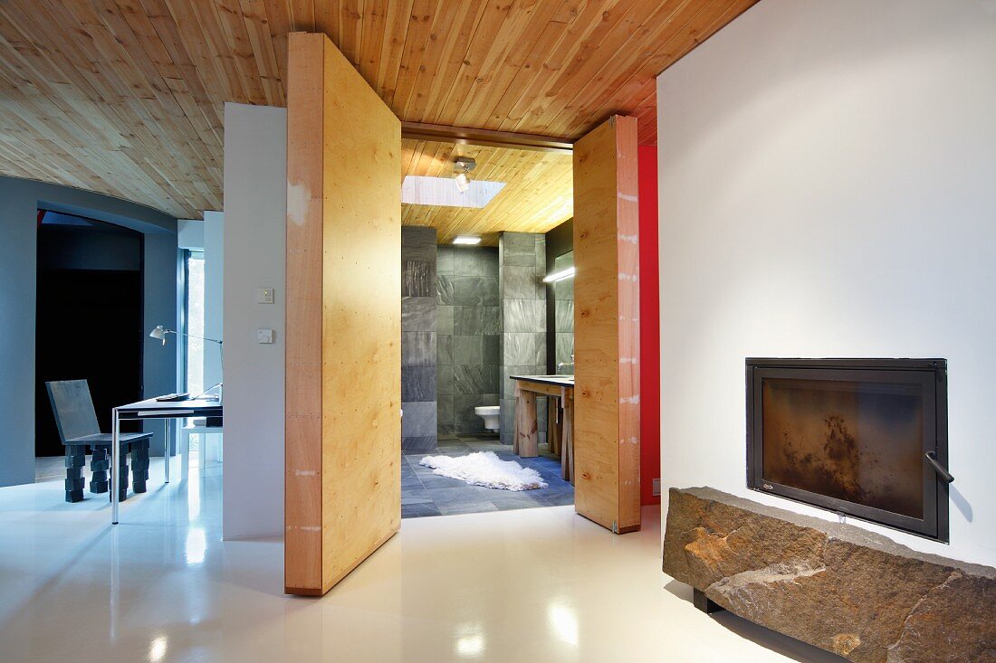 Stone slab below glass-fronted fireplace in open-plan, purist bedroom