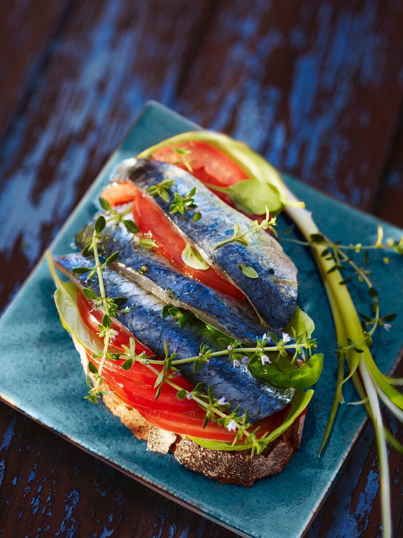 A sliced of bread topped with sardines and tomatoes