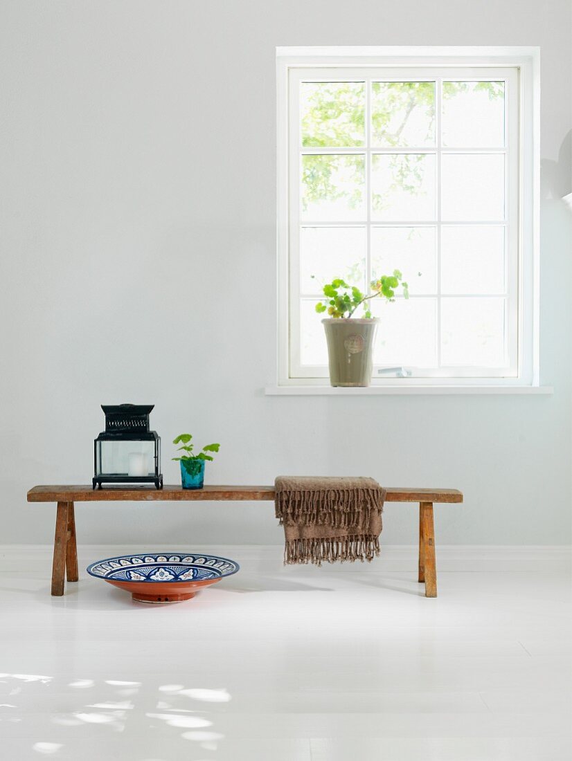 Lantern on rustic wooden bench and ceramic bowl on white wooden floor below lattice window