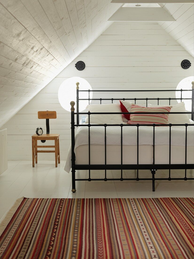 Striped rug in front of double bed with black metal frame in wood-clad niche in attic