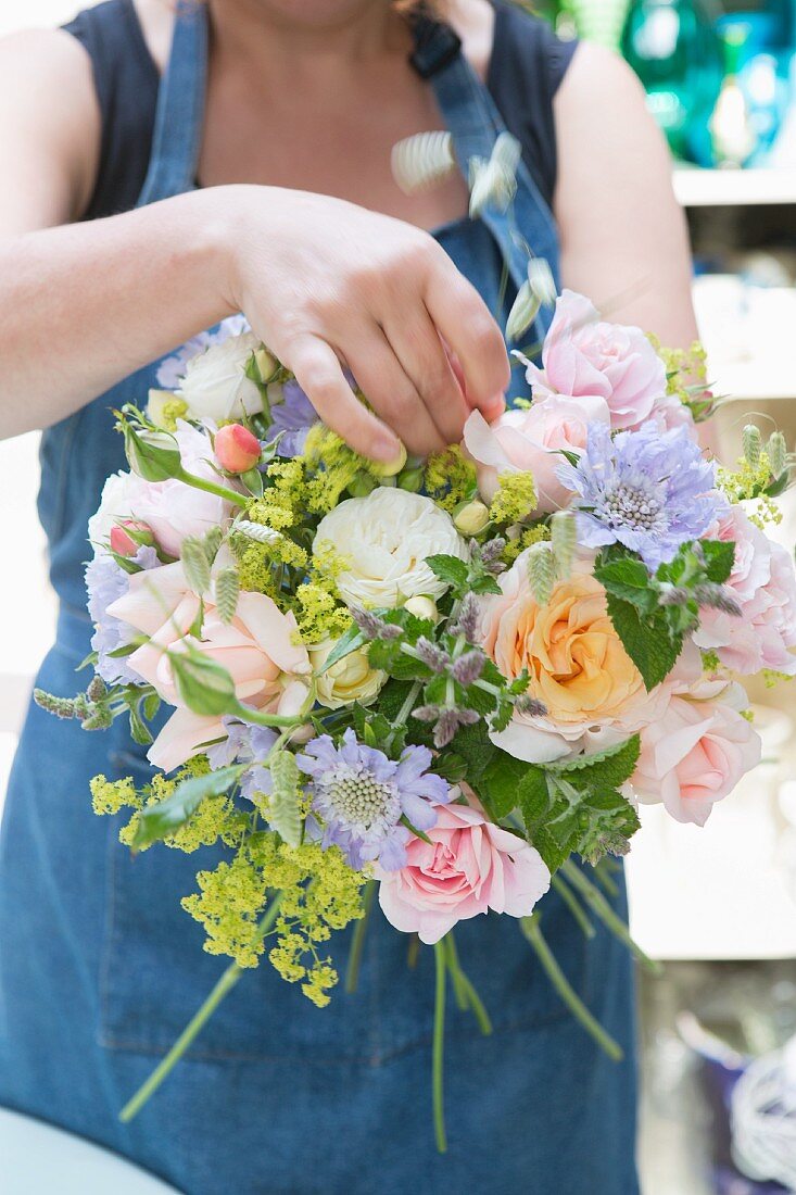 Frau bindet Blumenbouquet aus Rosen & Scabiosen