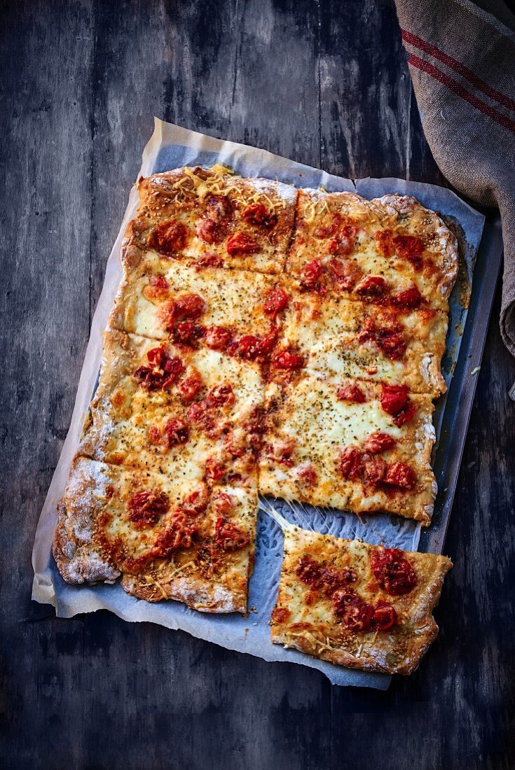 Pizza mit Käse und Tomaten geschnitten auf dem Backblech