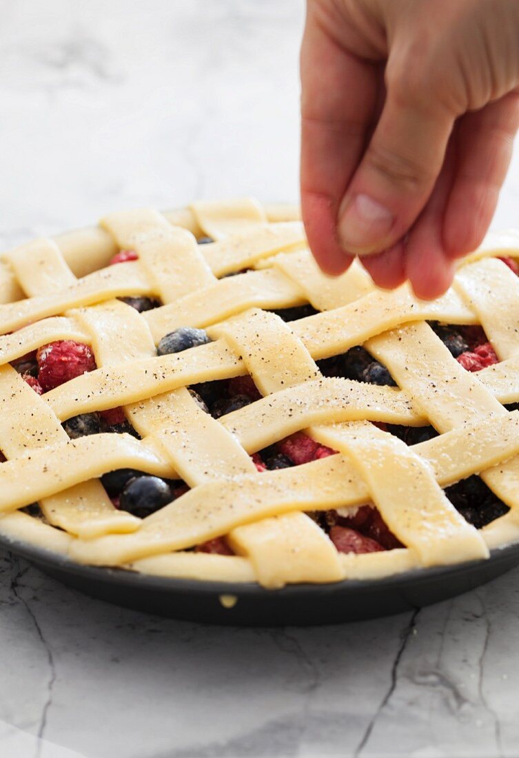 An unbaked berry pie being sprinkled with vanilla sugar