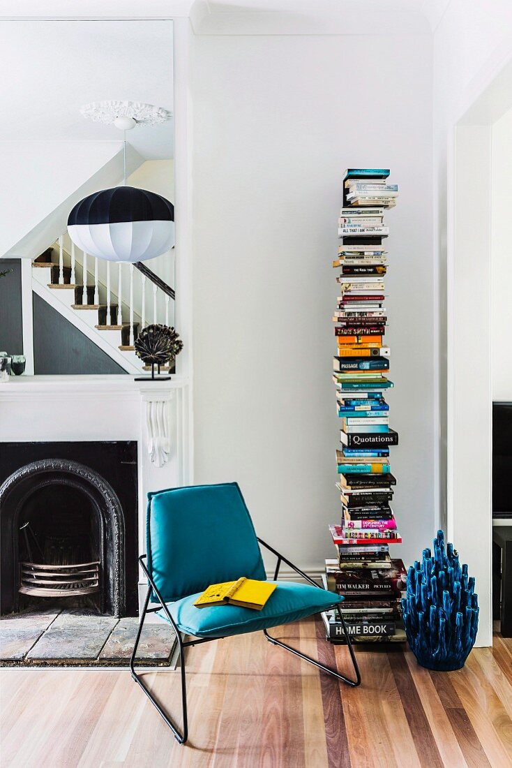 Moderne Leseecke mit Designer-Bücherregal vor offenem Kamin, Kaminspiegel und gespiegelter Holztreppe