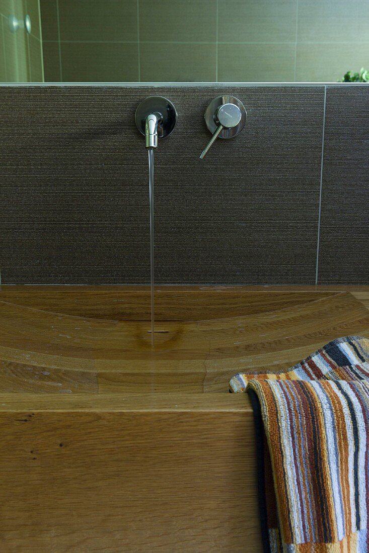 Elegant wooden washstand with carved sink, striped towel and water running from wall-mounted tap