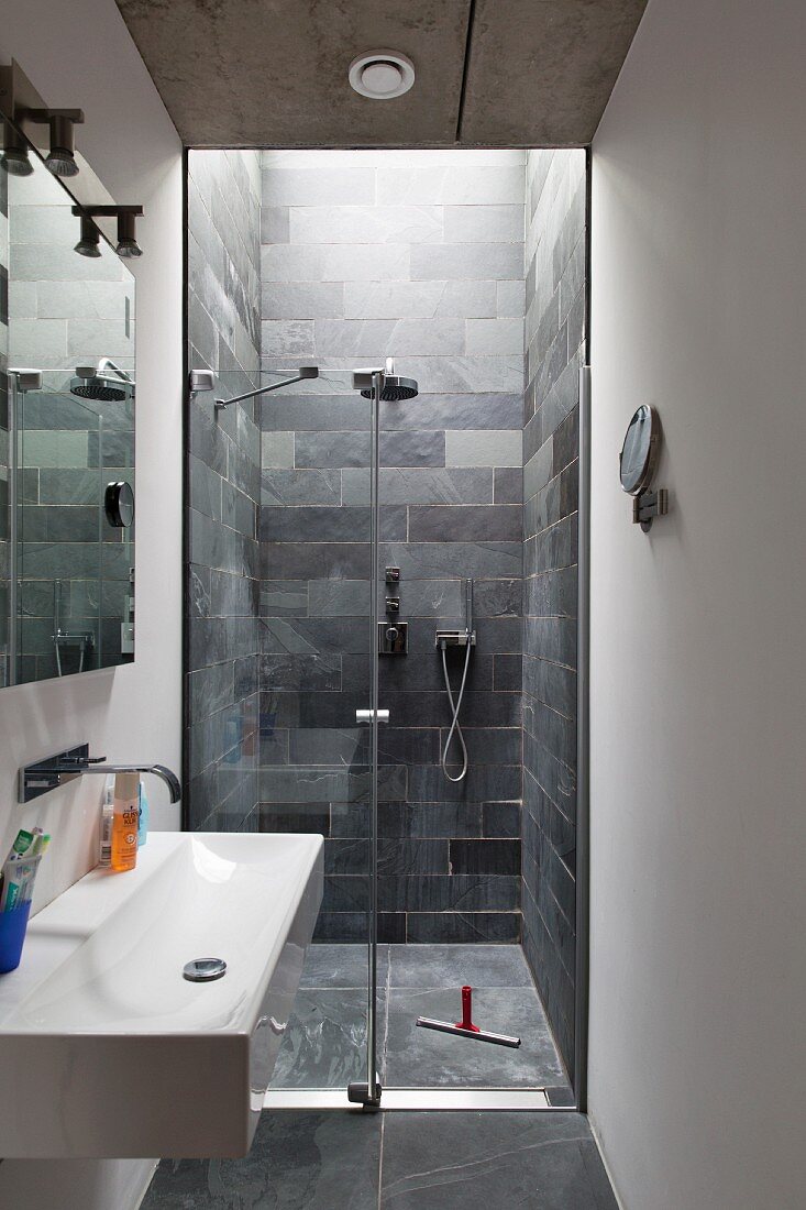 Sink with wall-mounted tap and floor-level shower area with slate-tiled walls in narrow modern bathroom