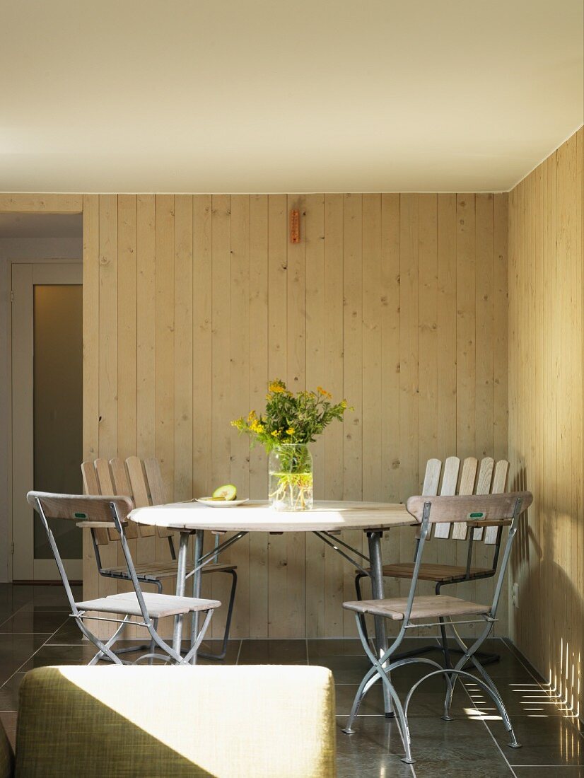 Round table and garden chairs in corner of wood-clad room