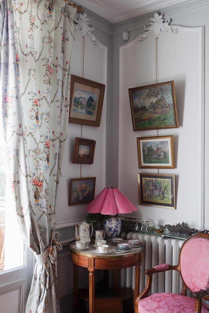 Runder Beistelltisch im Rokoko Stil in Zimmerecke, oberhalb an Wand aufgehängte Bilder