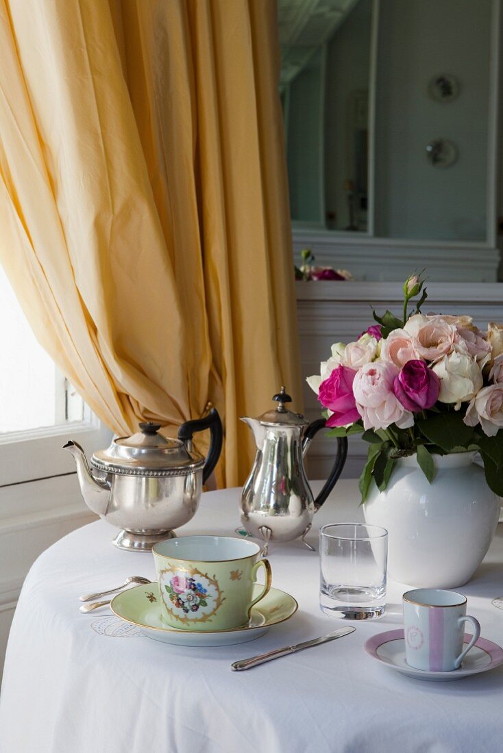 Tasse und Silberkannen neben Blumenstrauss auf rundem Tisch
