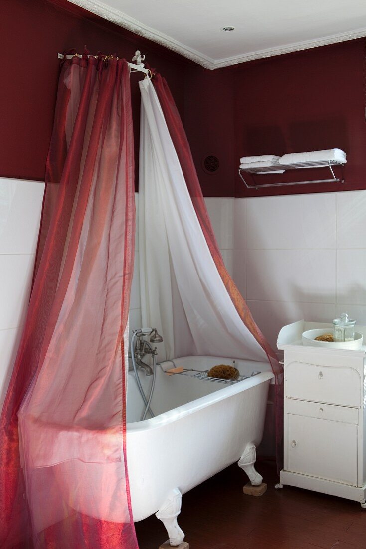 Freistehende Vintage Badewanne auf Löwenfüssen, oberhalb Baldachin mit rotem und weißem Stoff