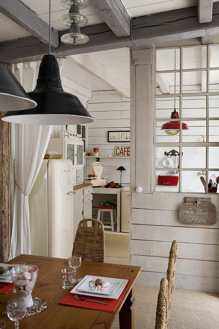Esstisch aus Holz, oberhalb Pendelleuchten, im Hintergrund Trennwand vor Küche mit Sprossenverglasung