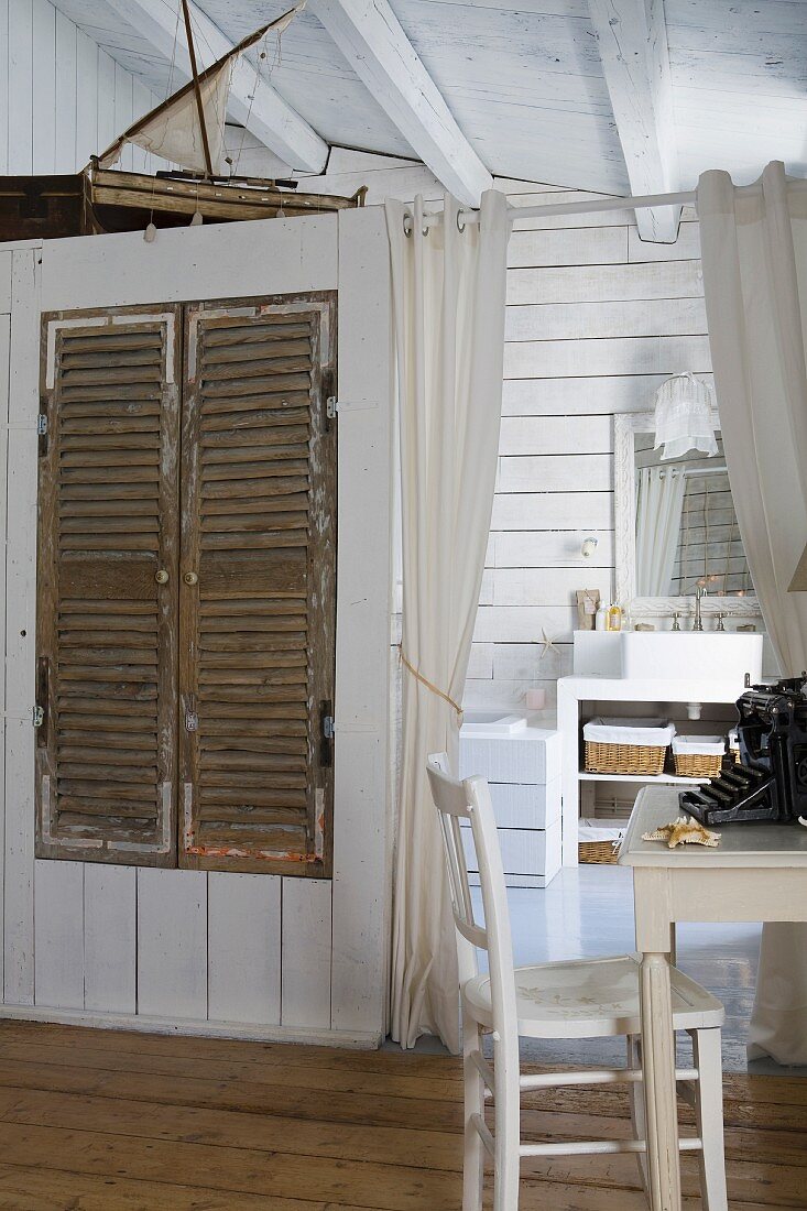 White-painted desk and chair in front of doorway leading to ensuite bathroom with rustic fitted wardrobe in partition