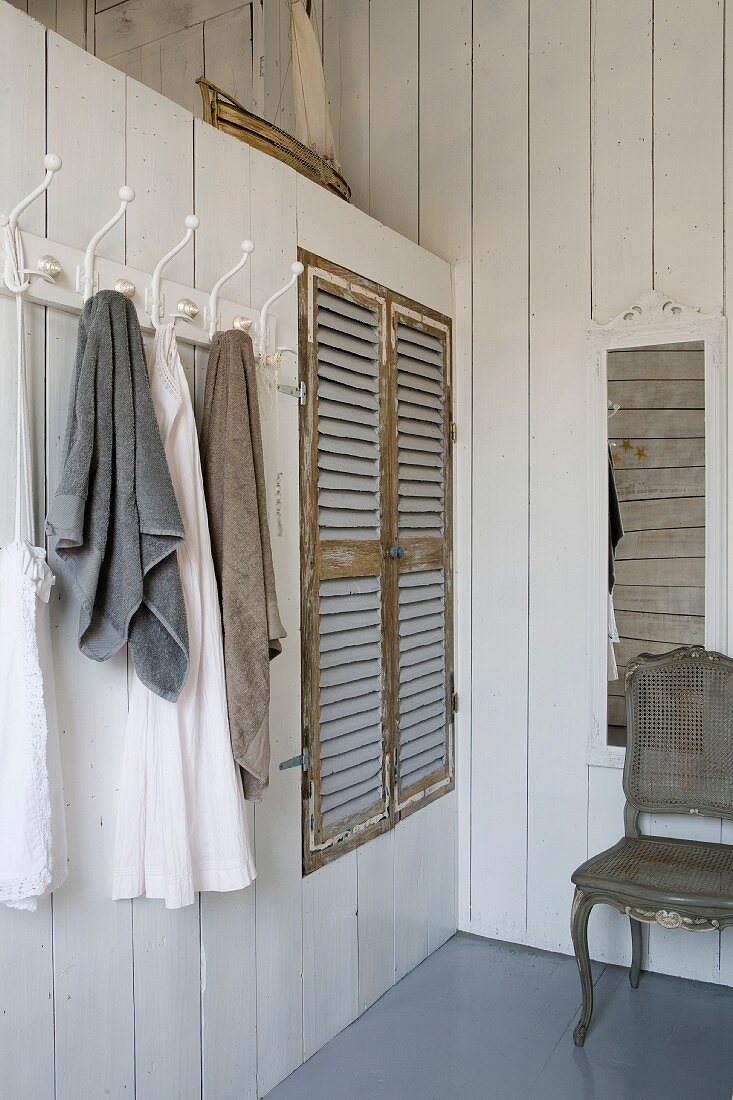 Towels hanging on row of coat hooks next to fitted wardrobe with rustic louvre doors in white wood-clad partition