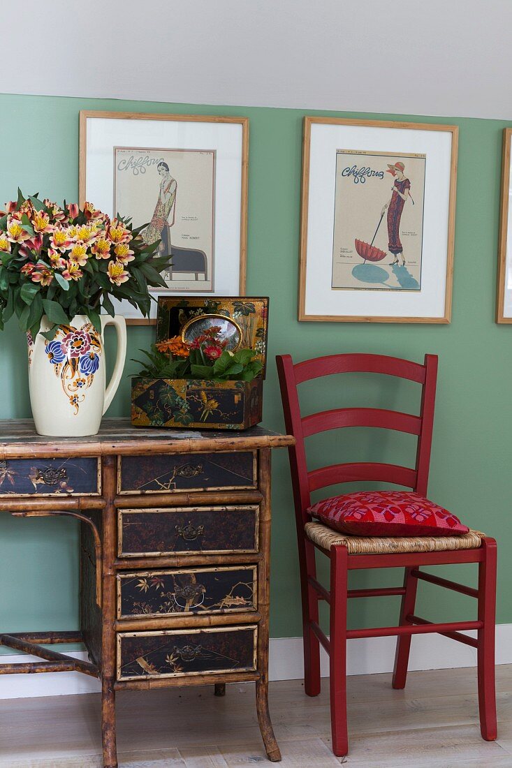 Red kitchen chair next to antique desk with bamboo frame below retro pictures on green wall
