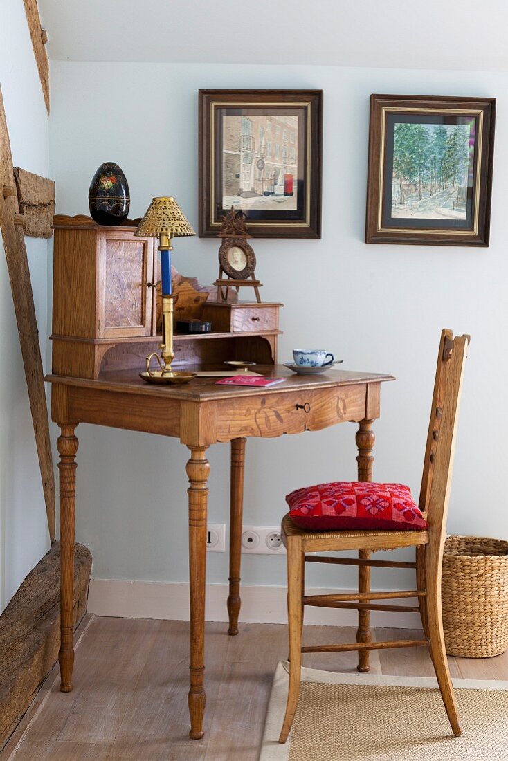 Simple wooden chair at antique bureau with turned legs in corner of room