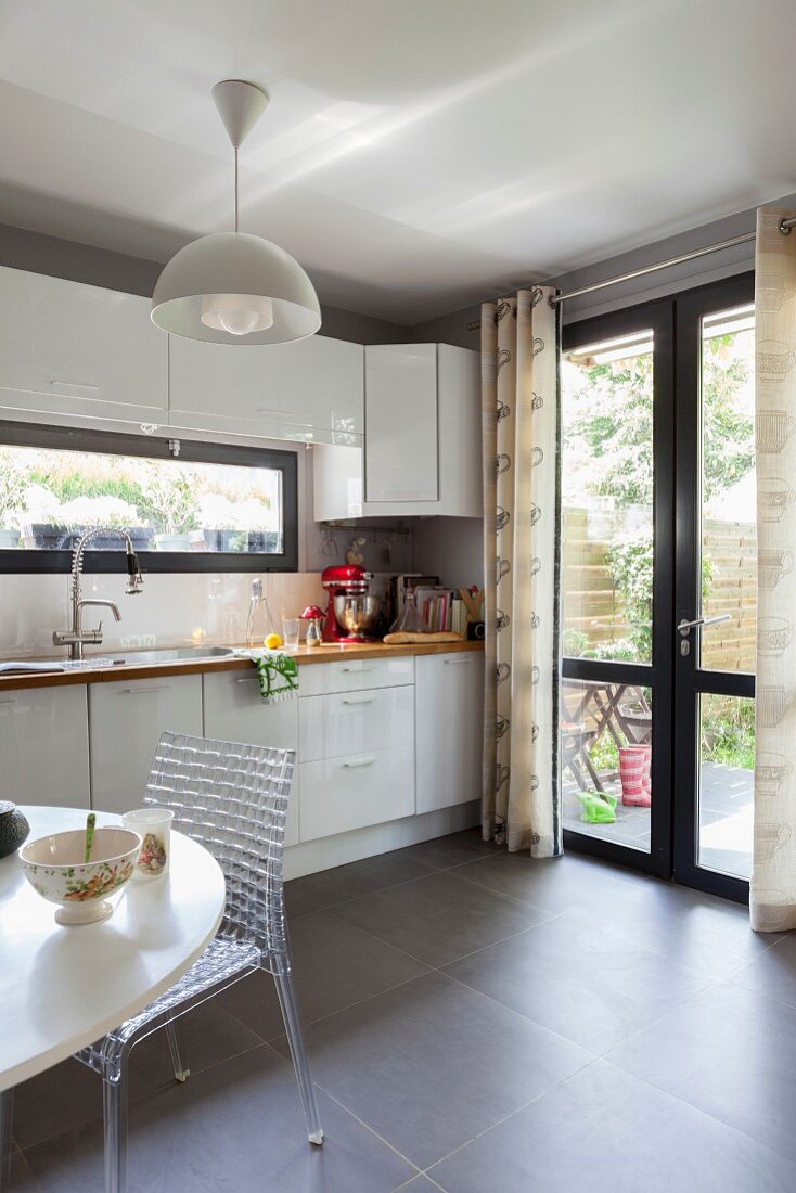 Designer chair at table next to white kitchen counter with French windows in background