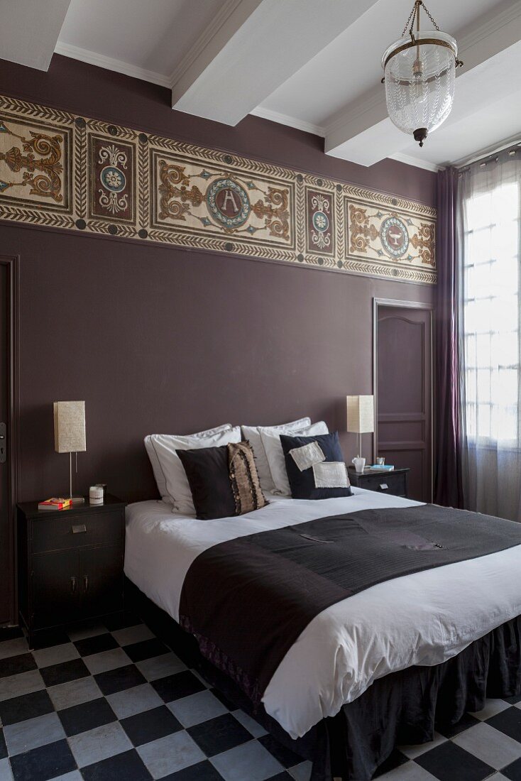 Double bed in bedroom with chequered floor and Art-Nouveau frieze on purple-painted wall