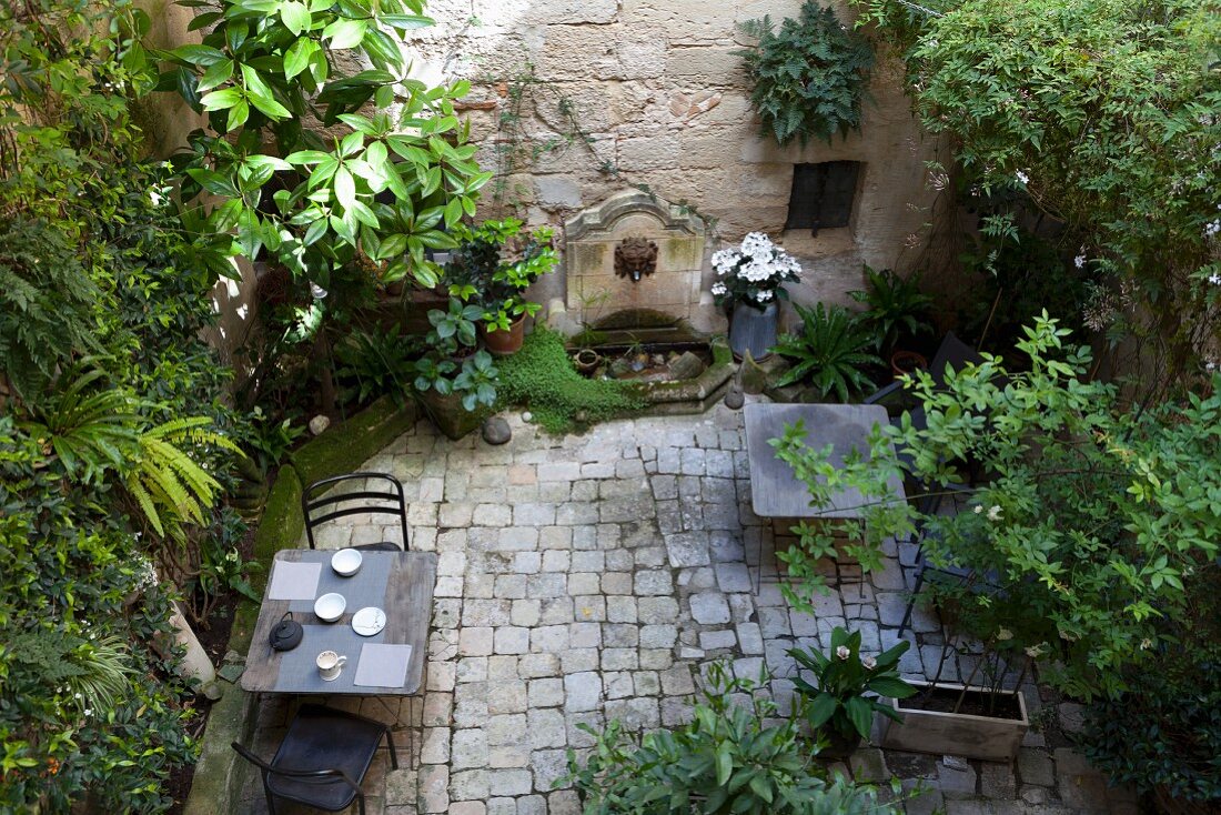 View down into planted courtyard with set table and chairs on paved floor