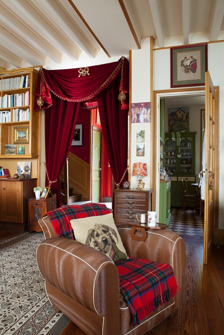 Antique furniture, curtain on doorway and dog-motif scatter cushion on leather armchair in classic living room