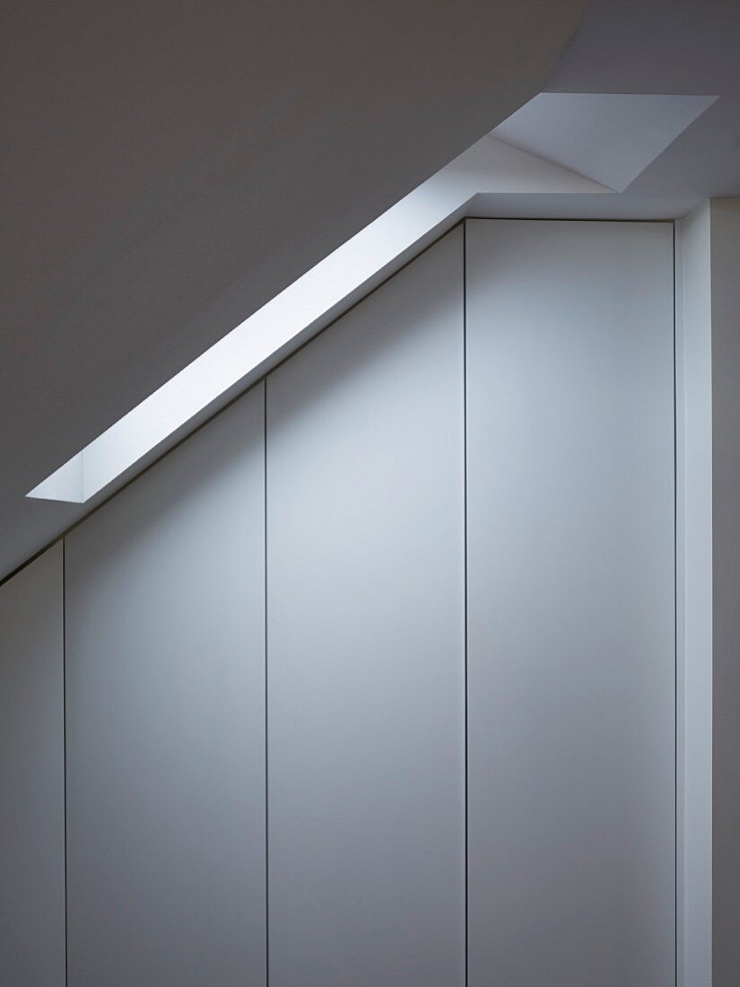 Simple fitted wardrobes without handles under sloping ceiling with skylight
