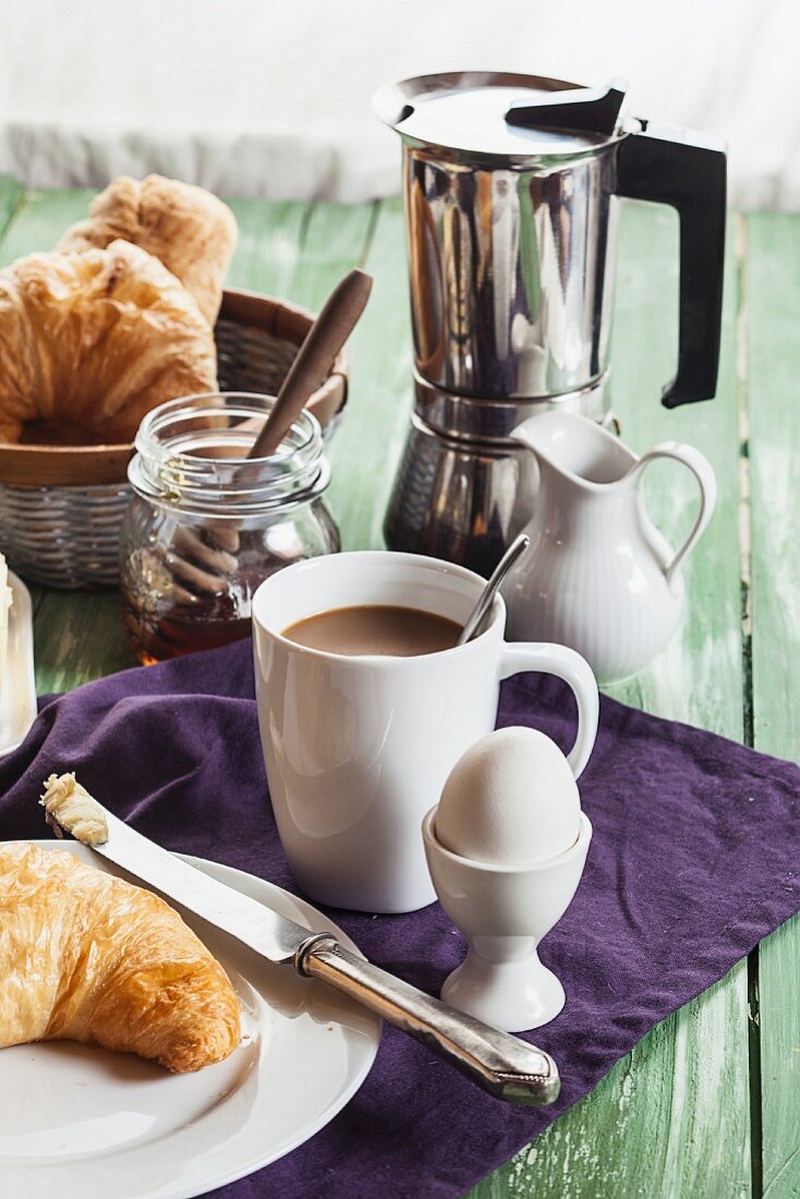 A breakfast with a croissant, coffee, egg and honey