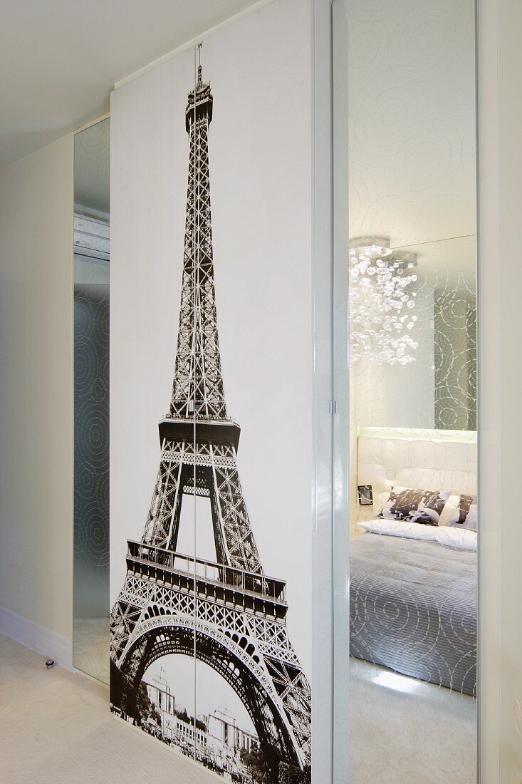 A black-and-white wall picture of the Eiffel Tower, flanked by mirrors reflecting an elegant bedroom