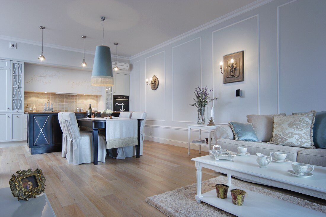 Elegant living-dining room in shades of pale blue and cream with open-plan fitted kitchen in background