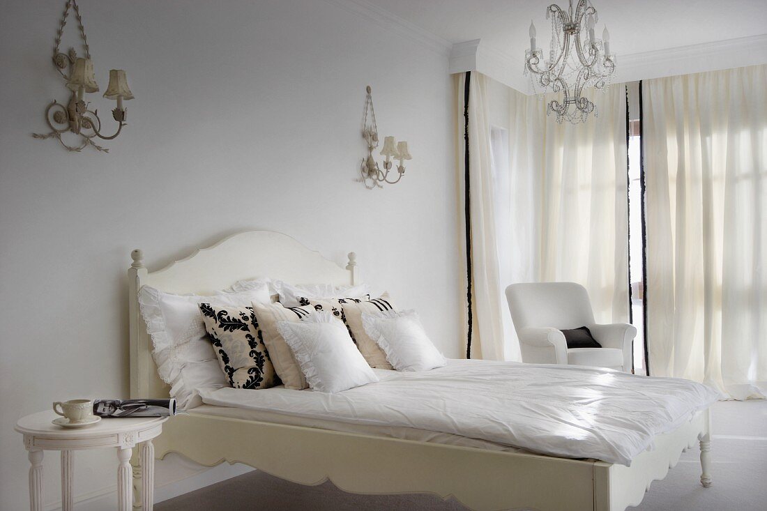 Elegant, white bedroom with period furniture, ornate sconce lamps and chandelier